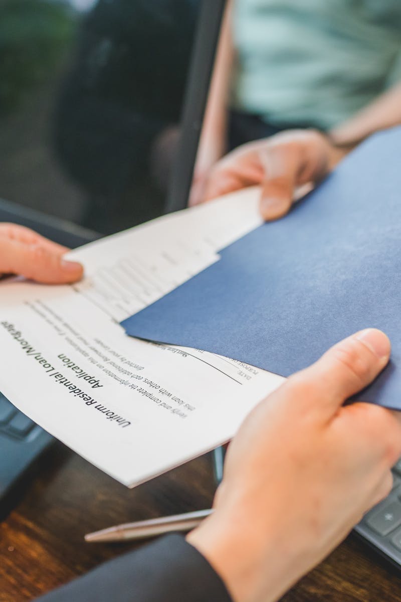 Close-up of hands exchanging real estate documents in an office setting.